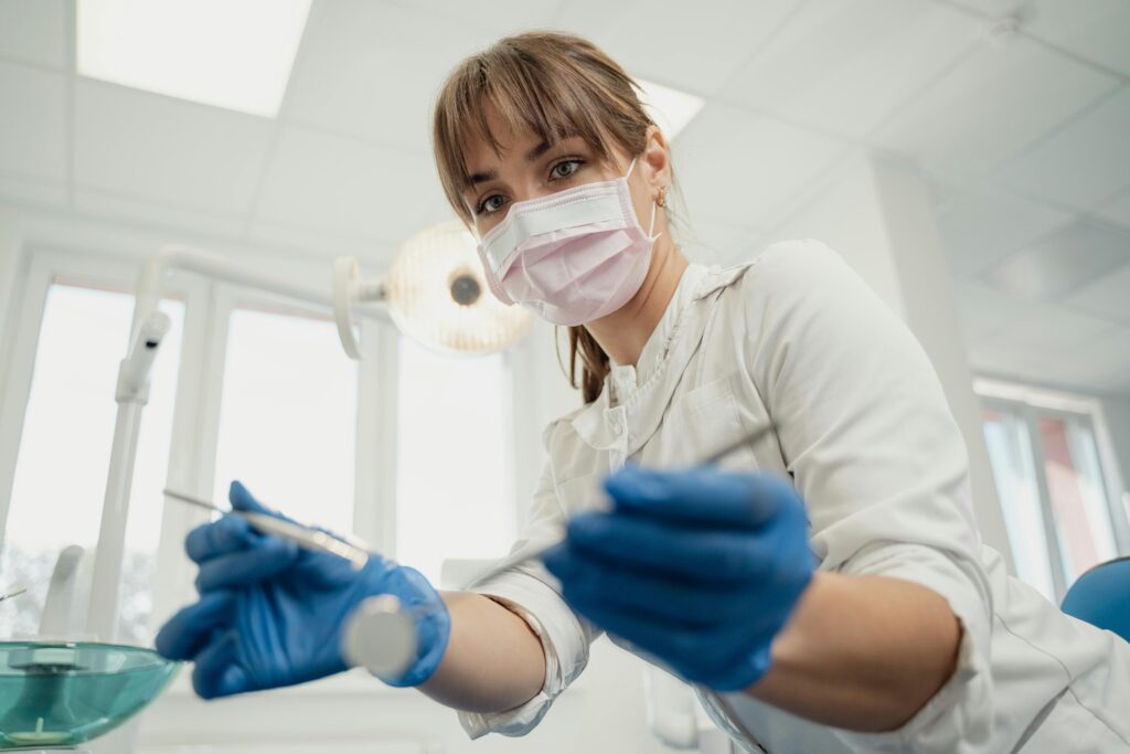 Dentist wearing mask and gloves holding dental tools.