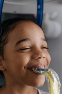 Child smiling with a dental tool in mouth.