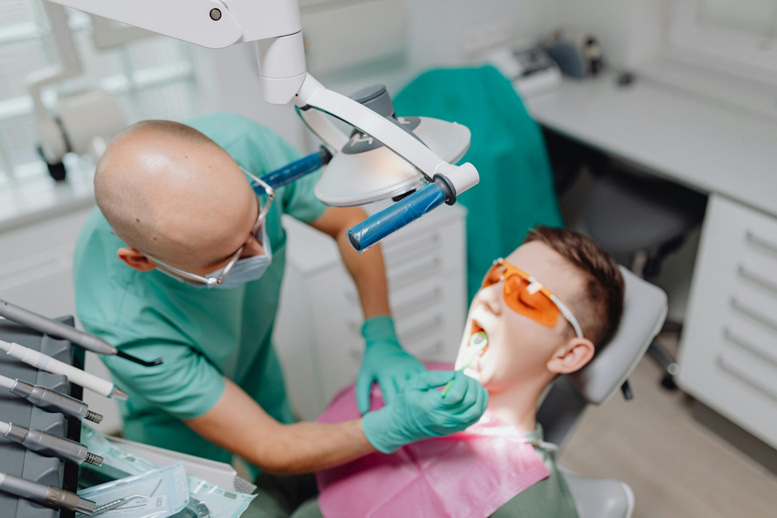 Dentist in green scrubs examining a patient in a dental chair.