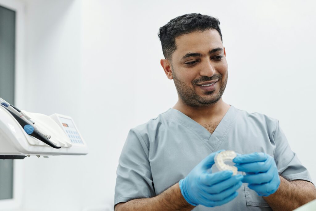 Dentist in scrubs holding a dental model in a clinic.