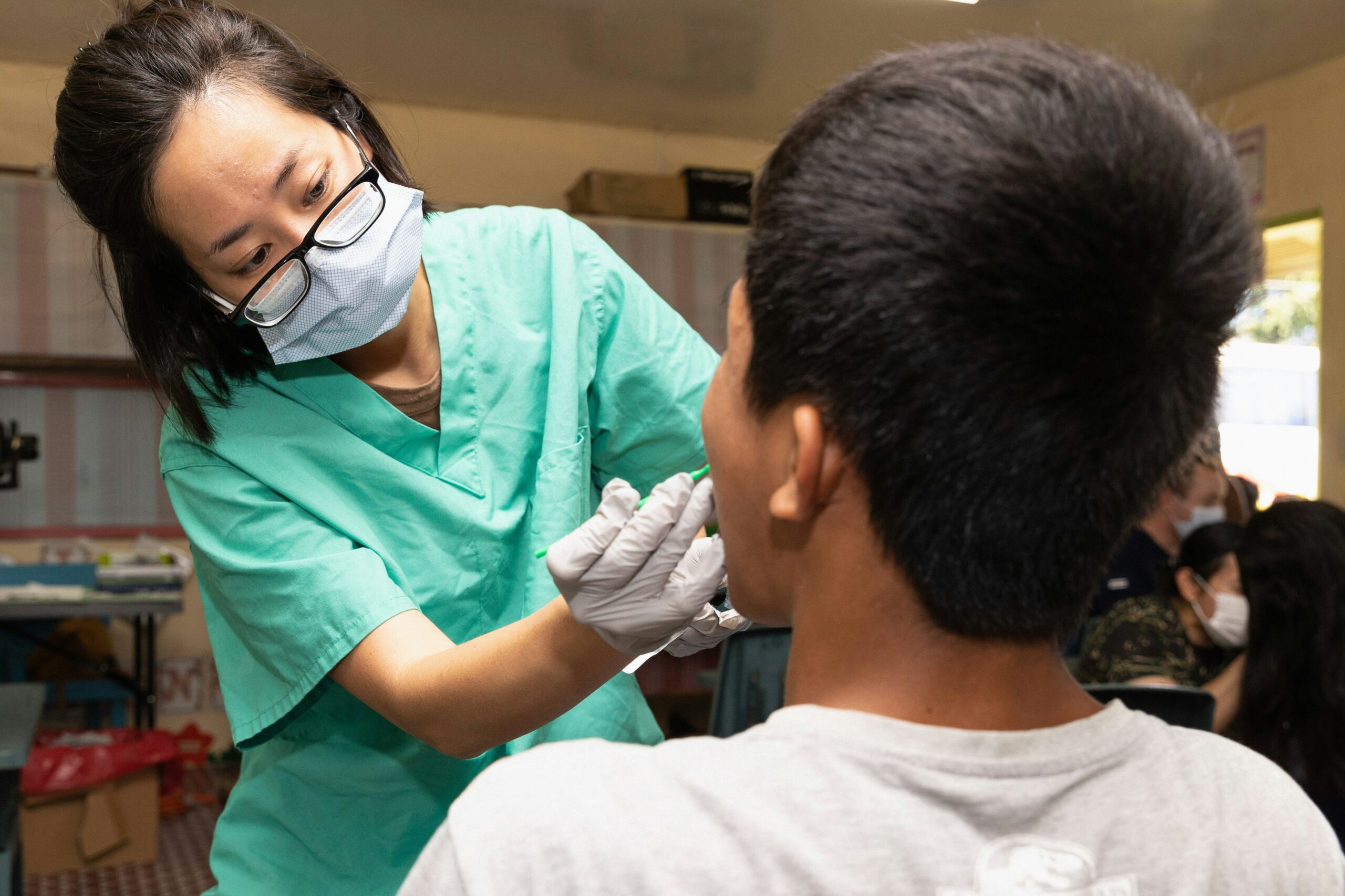 Dentist in green scrubs examining a patient's mouth.