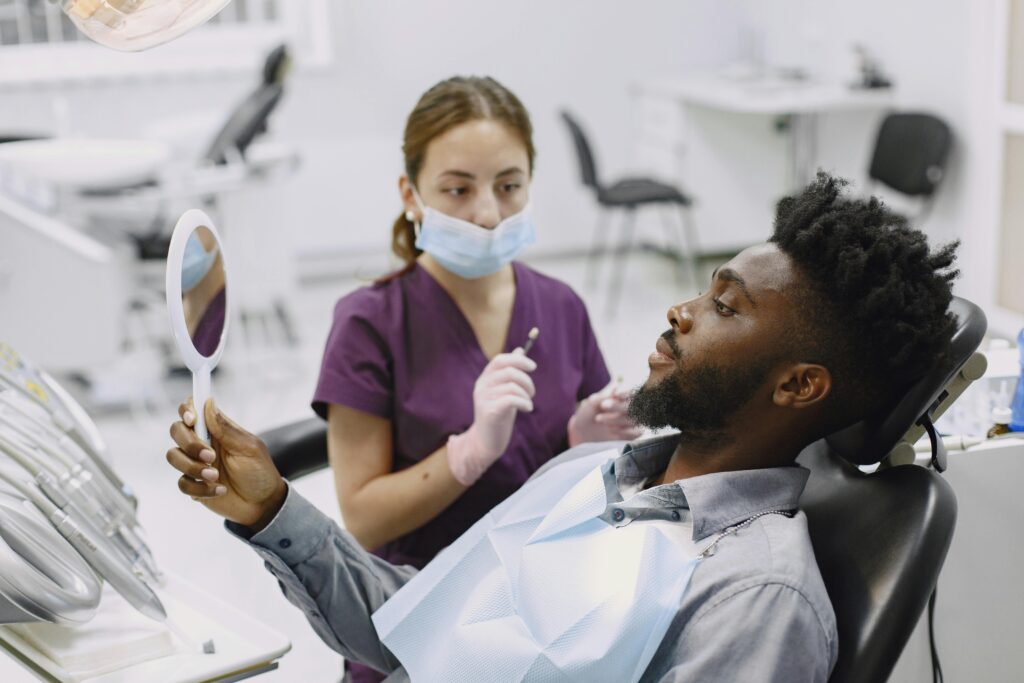 Patient holding a mirror in a dental chair with a dentist nearby.
