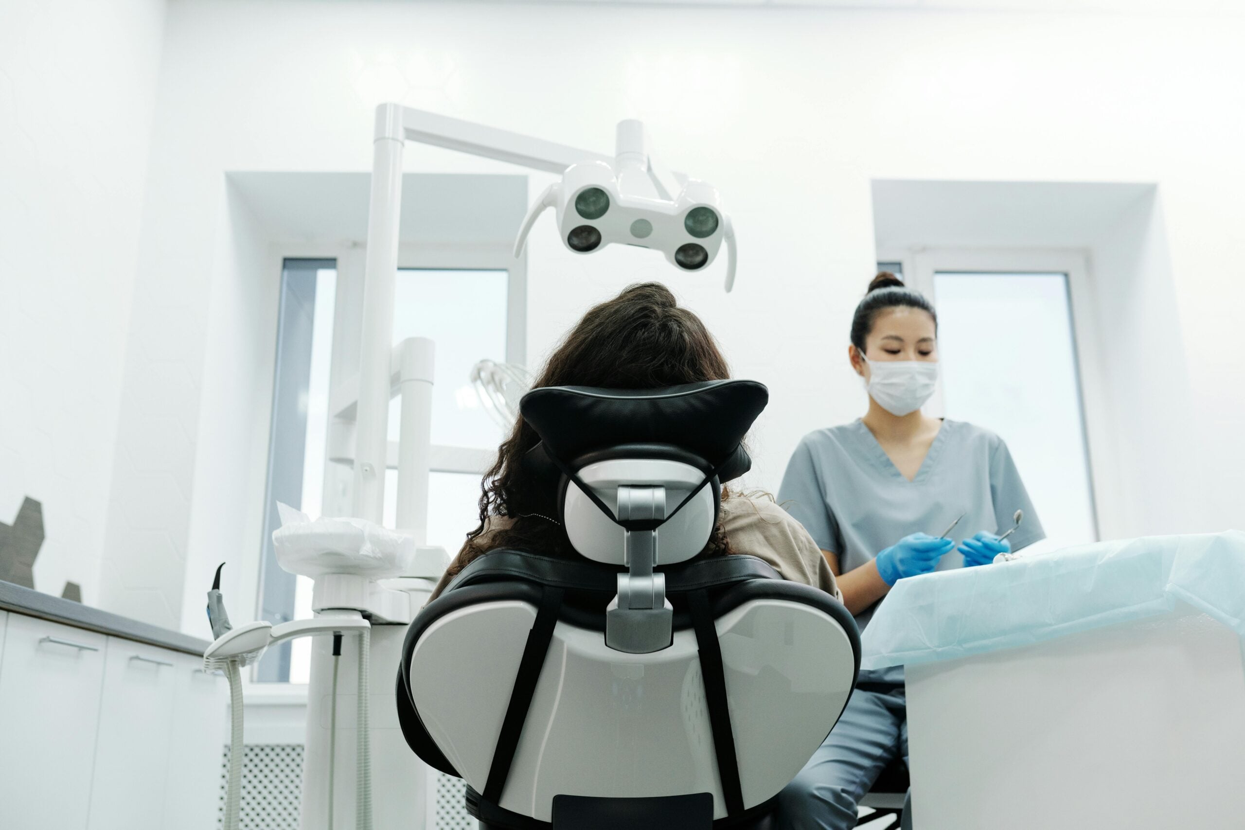 Dentist in scrubs with patient in dental chair.
